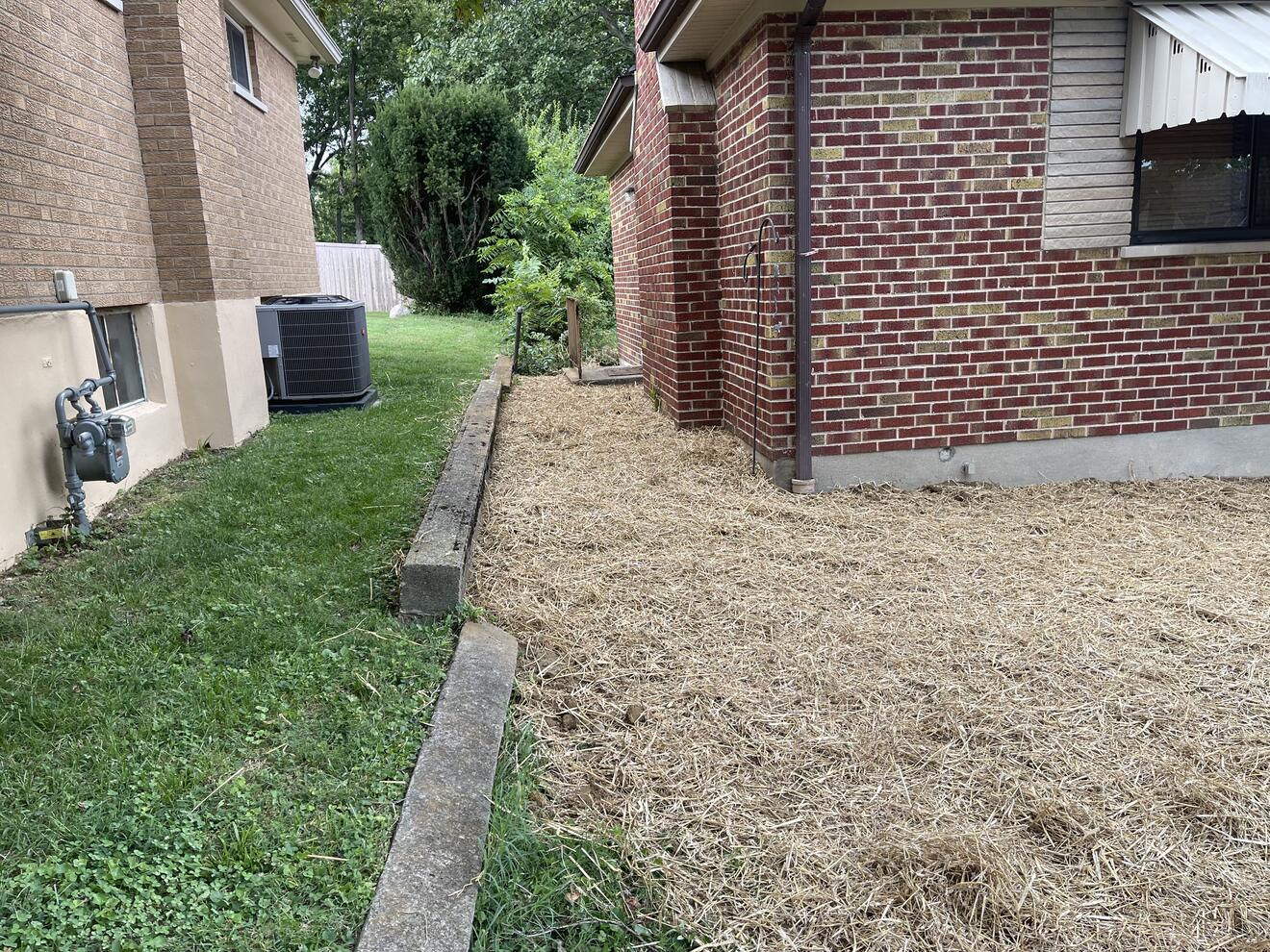 Side yard regraded along a brick foundation with a stone curb edge, pitched to carry runoff to daylight